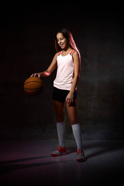 Beautiful caucasian teen woman in sportswear playing basketball . Sport concept isolated on black background. - Foto, immagini