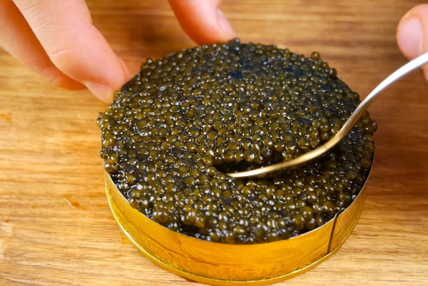 Black caviar in cardboard box. Spooning black caviar. - Photo, Image