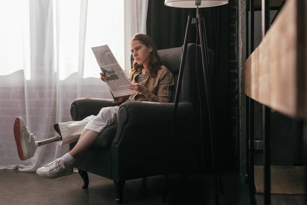 Protez bacaklı güzel bir kız evde gazete okuyor. - Fotoğraf, Görsel