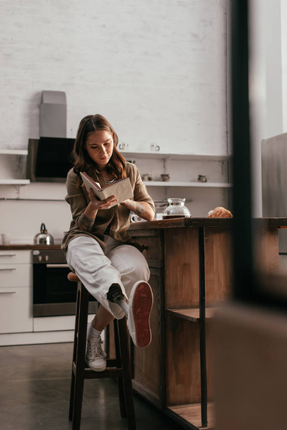 Красива жінка з протезною ногою читає книгу за кухонним столом
 - Фото, зображення