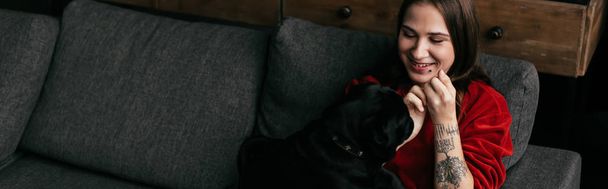 Panoráma felvétel mosolygós lány nézi mopsz kutya kanapén - Fotó, kép