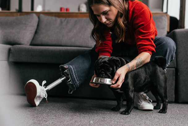Chica con la prótesis de la pierna de alimentación perrito en la sala de estar
 - Foto, imagen