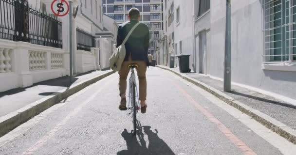 Rear view of a young Caucasian businessman on the go in the city, riding a bike in the street, slow motion - 映像、動画