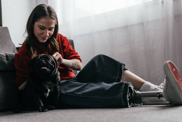 Girl with prosthetic leg petting pug on floor in living room - Photo, image