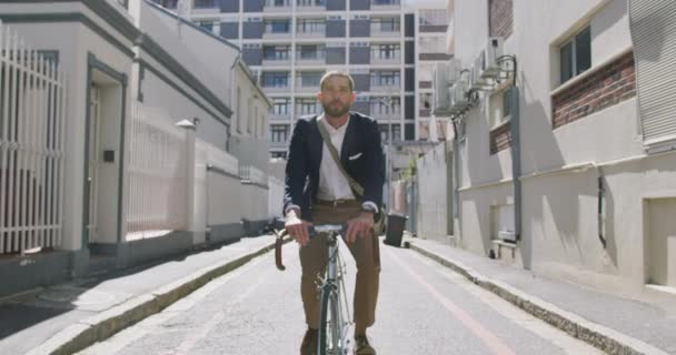 Front view of a young Caucasian businessman on the go in the city, riding a bike in the street, slow motion - Video