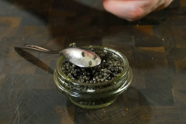 Ανακατεύοντας μαύρο χαβιάρι με κουτάλι σε γυάλινο βάζο. - Φωτογραφία, εικόνα