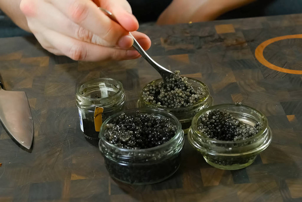 Roeren zwarte kaviaar met een lepel in glazen pot. - Foto, afbeelding