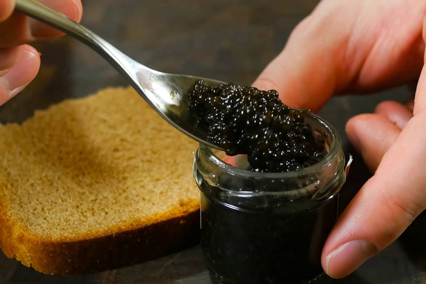 Agiter le caviar noir avec une cuillère dans un bocal en verre
. - Photo, image