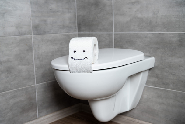 トイレの紙の上のスマイルサイングレーのタイルとバスルームの白いトイレ席 - 写真・画像