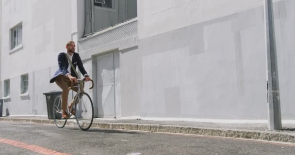 Side view of a young Caucasian businessman on the go in the city, riding a bike in the street, slow motion - Video