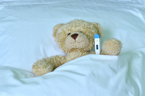 Teddy bear with a electronic thermometer in bed - Photo, Image