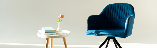 Panorâmica tiro de poltrona azul por mesa de café com flor em vaso e livros sobre fundo cinza
 - Foto, Imagem