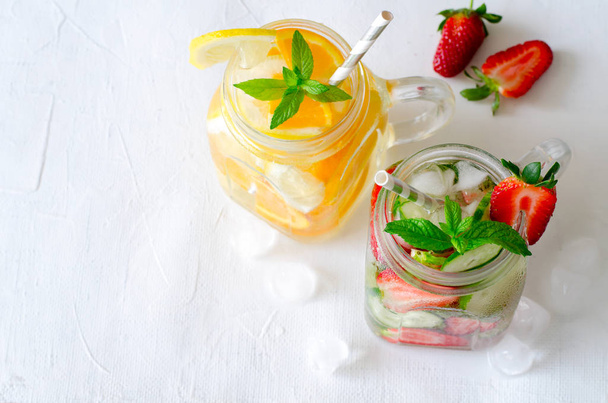 Summer refreshing iced drinks with orange, lemon, cucumber and strawberry on white background - Фото, зображення