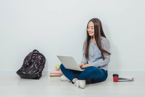 Lovely young asian lady sitting on the floor in lotos position, searching something in her laptop, smiling. School supplies around her. - Φωτογραφία, εικόνα