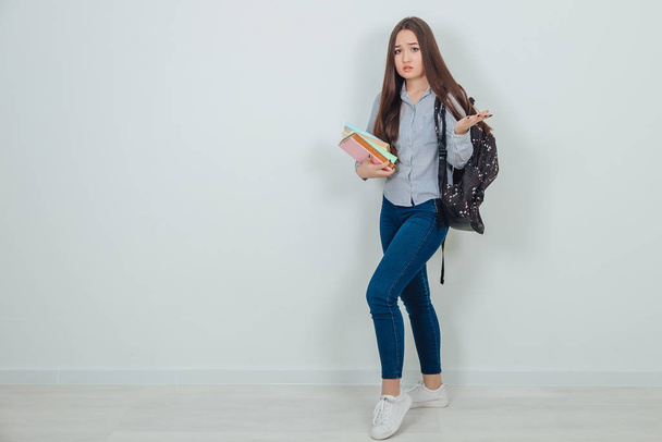 Felice casuale ragazza asiatica studente con zaino in piedi con pila di libri, gettando una mano, malinteso sul suo viso
. - Foto, immagini