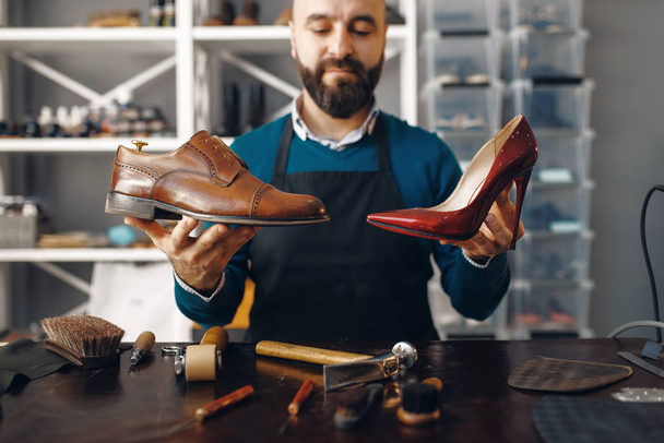 Bootmaker toont gerepareerde schoenen, schoeisel reparatie service. Vakmanschap, schoenmakerij, meesterwerken met laarzen, schoenmakerij - Foto, afbeelding