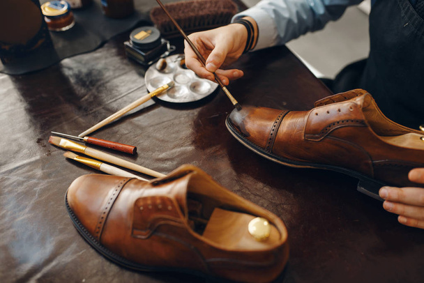Bootmaker met borstel tinten schoenen, schoeisel reparatie service. Vakmanschap, schoenmakerij, schoenenwinkel - Foto, afbeelding