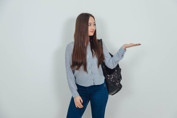 Inspired young asian girl standing with backpack slung over her shoulder, raising her opened palm with copyspace for text or product. - Foto, Imagen