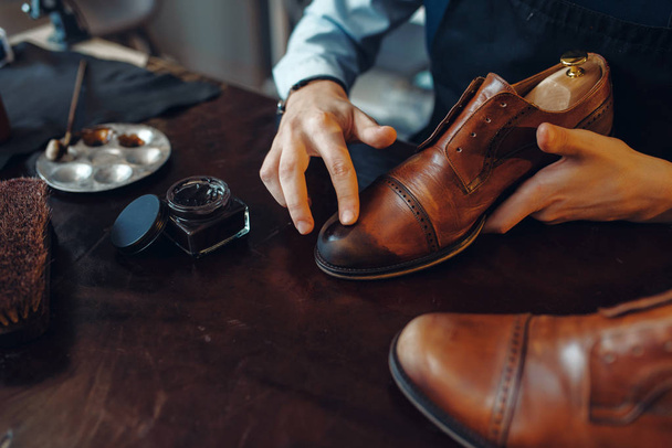 Shoemaker applies black shoe polish, footwear repair service. Craftsman skill, shoemaking workshop, master works with boots, cobbler shop - Foto, Imagem
