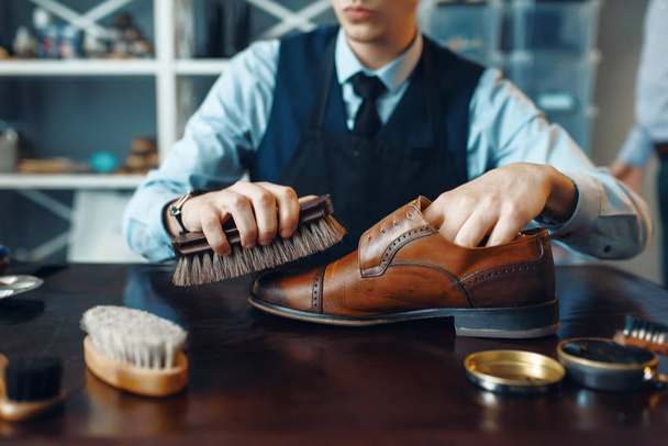 Shoemaker wipes black shoe polish, footwear repair service. Craftsman skill, shoemaking workshop, master works with boots, cobbler shop - Photo, image