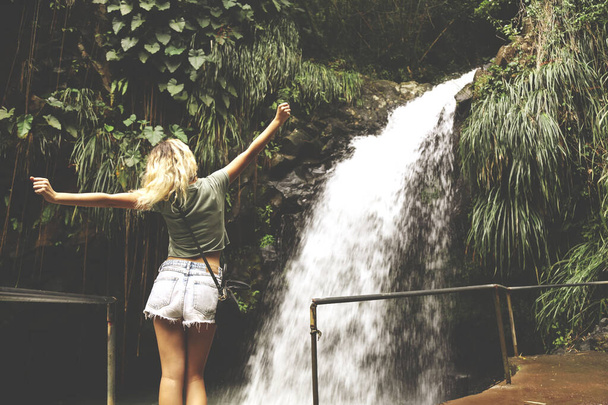 Frau steht mit erhobenen Händen vor Wasserfall. - Foto, Bild
