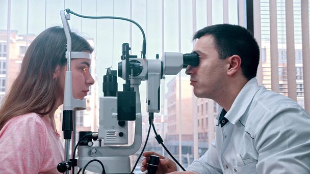 Офтальмологія - молода красива жінка перевіряє гостроту зору за допомогою спеціального обладнання у просторому кабінеті
 - Фото, зображення