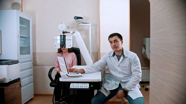 Офтальмологія - молода жінка перевіряє гостроту зору за допомогою обладнання оптометрів - лікар сидить поруч
 - Фото, зображення