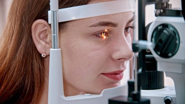Traitement ophtalmologique - une jeune jolie femme vérifiant son acuité visuelle avec une lumière d'une grande machine d'optométrie spéciale - couleur des yeux marron
 - Photo, image