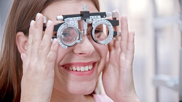 Tratamento oftalmológico - uma jovem mulher sorrindo colocando em um dispositivo para teste de visão
 - Foto, Imagem