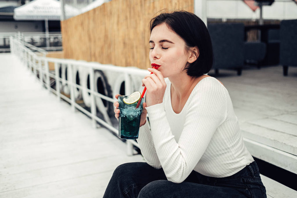 Зблизька Портрет красивої дівчини з Брюнета у білому светрі випиває коктейль у кафе біля озера - Фото, зображення
