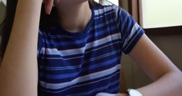 Front view close up of a bored teenage Caucasian schoolgirl sitting at a desk in class leaning on her hand and looking out of the window, with classmates working in the background, slow motion - 映像、動画