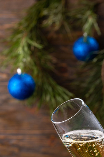Glass of champagne with bubbles on a background of Christmas decoration. Beautiful greeting card. - Фото, зображення