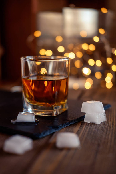 Een glas whisky of rum met ijs op een donkere en bokeh achtergrond - Foto, afbeelding