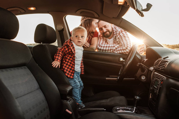 Šťastná mladá rodina maminka a tatínek s jejich syn malý řidič těší letní víkend piknik na autě mimo město na poli při slunečném dni západ slunce, dovolená a silniční výlet koncepce - Fotografie, Obrázek