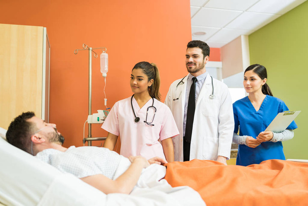 Médicos e enfermeiros que olham para o doente médio adulto enquanto estão de pé no hospital
 - Foto, Imagem