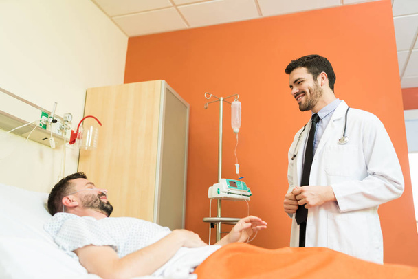 Low angle view of smiling mid adult doctor talking to male patient at hospital - Photo, Image