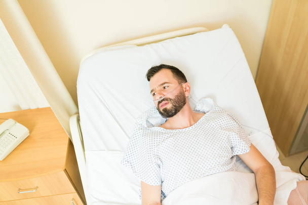 Przemyślany chory pacjent odwraca wzrok leżąc na szpitalnym łóżku podczas leczenia - Zdjęcie, obraz