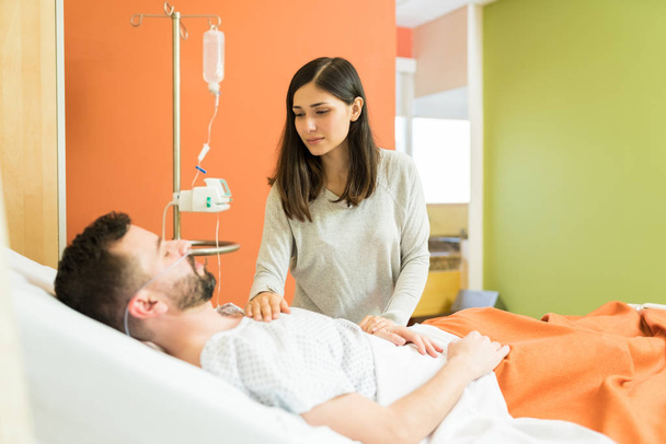 Γυναίκα παρηγορεί τον άντρα ενώ στέκεται δίπλα στο κρεβάτι στο νοσοκομείο - Φωτογραφία, εικόνα