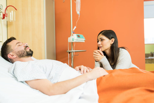 Mujer triste rezando mientras mira al hombre inconsciente durante la visita al hospital
 - Foto, Imagen
