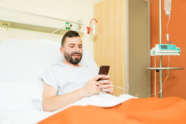 Latynoski pacjent korzystający ze smartfona podczas odpoczynku na łóżku w szpitalu - Zdjęcie, obraz