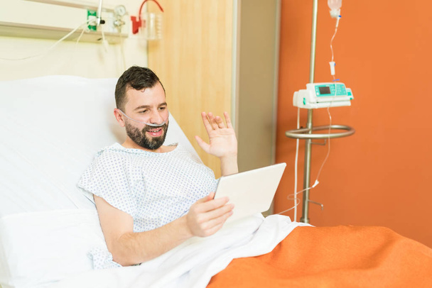 Hymyilevä miespotilas vilkuttaa videoneuvottelun aikana digitaalisella tabletilla sairaalassa
 - Valokuva, kuva