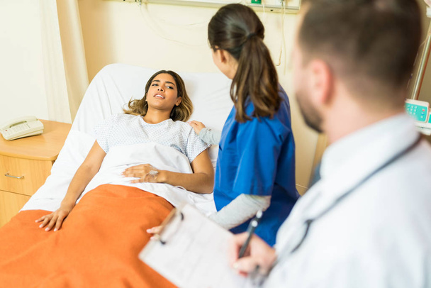 Verpleegster in gesprek met patiënt terwijl arts rapporten op klembord in het ziekenhuis - Foto, afbeelding