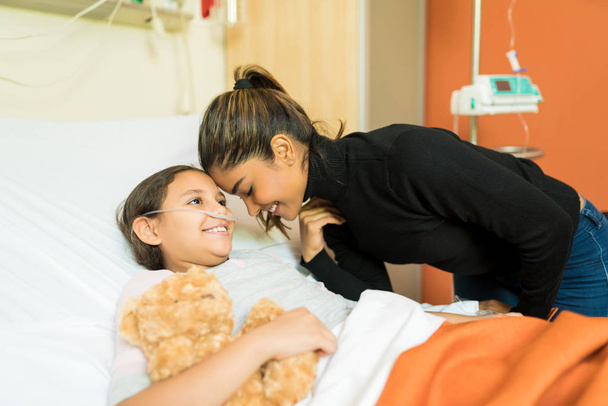 Mosolygó anya és beteg lánya az ágyban a kórházban látogatás közben - Fotó, kép