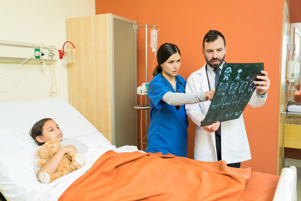 Gesundheitshelfer schauen sich Röntgenbilder an, während sie über Patienten diskutieren, die im Krankenhaus auf dem Bett liegen - Foto, Bild
