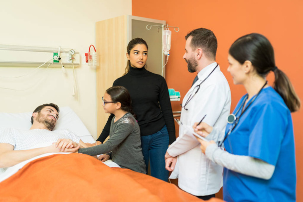 Врач и медсестра объясняют болезнь женщине, стоя рядом с больным человеком в больнице
 - Фото, изображение