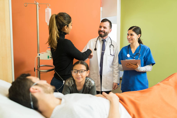 Mulher apertando as mãos com médico enquanto filha conversando com pai doente durante visita no hospital
 - Foto, Imagem