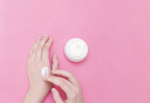Hands of a beautiful well-groomed woman with a cream jar on a pink textural background. Moisturizer for clean and soft skin in the winter. I love the body. Healthcare concept. - 写真・画像