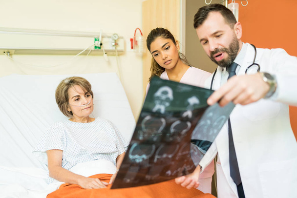 Profissionais de saúde do sexo masculino e feminino que explicam o diagnóstico por raio-x ao paciente idoso que sofre de problemas respiratórios no hospital
 - Foto, Imagem