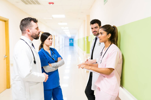 Male and female doctors and nurses discussing in meeting while standing in hospital corridor - Foto, Imagem