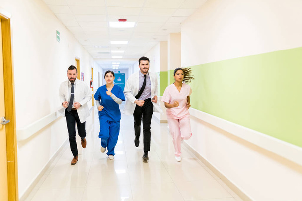 Huolestuneet mies- ja naislääkärit ja sairaanhoitajat juoksevat käytävällä sairaalassa hätätilanteessa
 - Valokuva, kuva